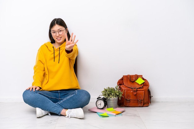 Young Chinese student woman sitting on the floor isolated on white wall happy and counting four with fingers