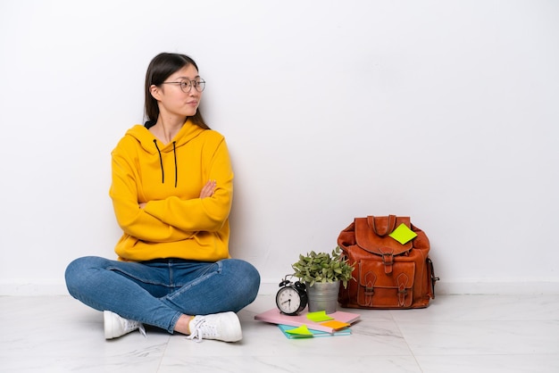 Young Chinese student woman sitting on the floor isolated on white wall in lateral position