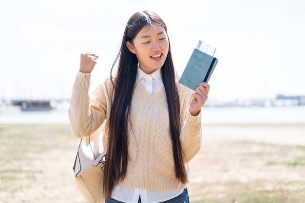 Young Chinese woman holding a passport at outdoors celebrating a victory