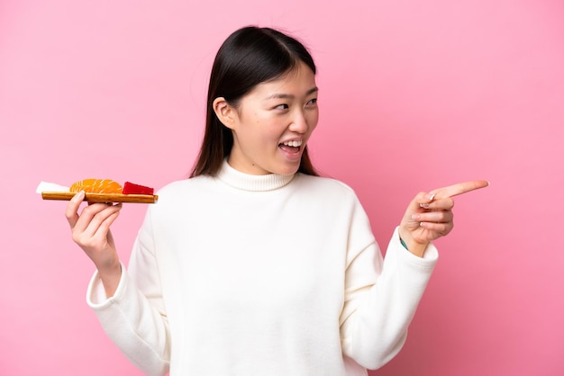 Young Chinese woman holding sashimi isolated on pink background pointing finger to the side and presenting a product