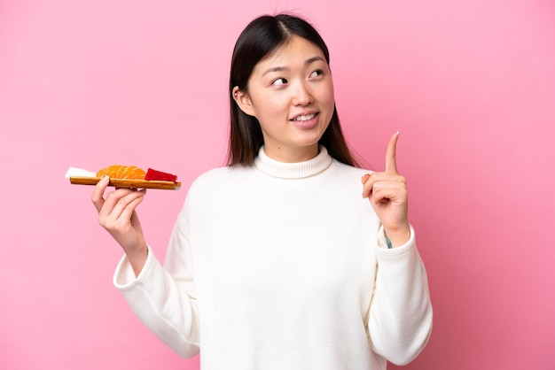 Young Chinese woman holding sashimi isolated on pink background pointing up a great idea