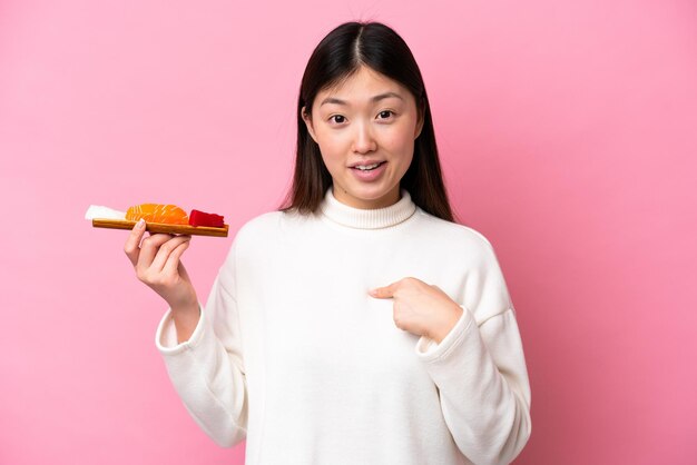 Young Chinese woman holding sashimi isolated on pink background with surprise facial expression