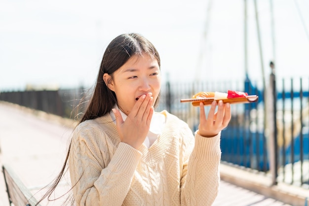 Young Chinese woman holding sashimi at outdoors with surprise and shocked facial expression