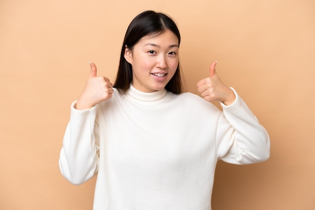 Young Chinese woman isolated on beige background giving a thumbs up gesture