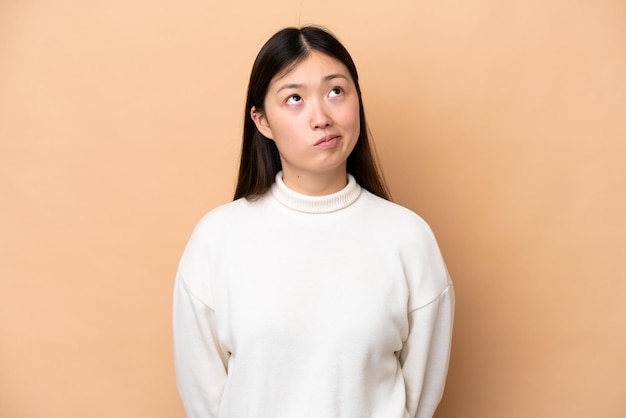 Young Chinese woman isolated on beige background and looking up