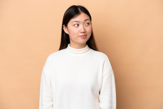 Young Chinese woman isolated on beige background making doubts gesture looking side