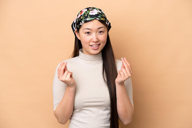 Young Chinese woman isolated on beige background making money gesture