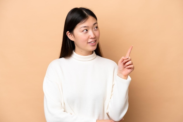 Young Chinese woman isolated on beige background pointing up a great idea