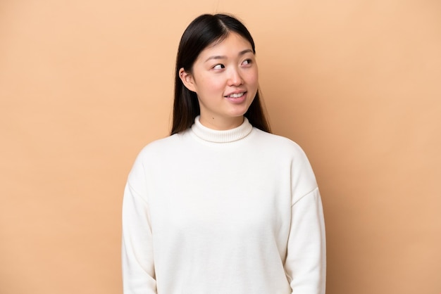 Young Chinese woman isolated on beige background thinking an idea while looking up