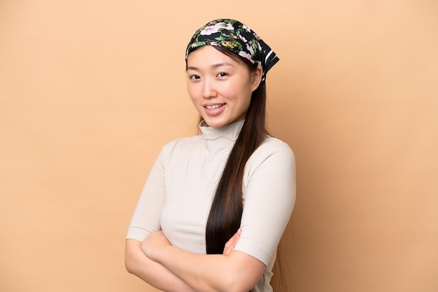 Young Chinese woman isolated on beige background with arms crossed and looking forward