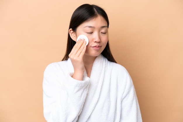 Young Chinese woman isolated on beige background with cotton pad for removing makeup from her face