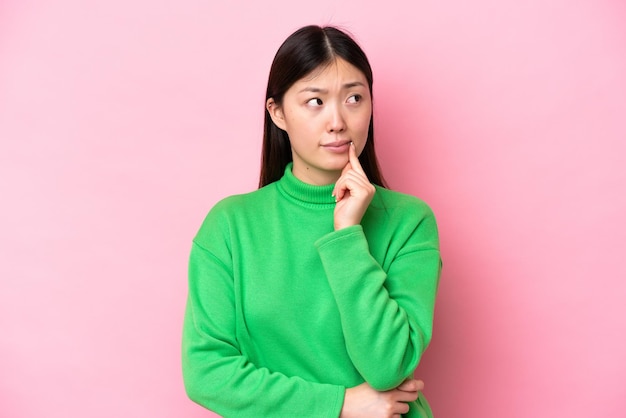 Young Chinese woman isolated on pink background having doubts and thinking