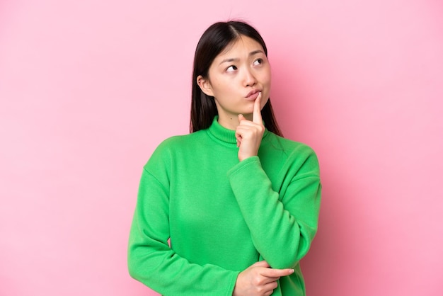 Young Chinese woman isolated on pink background having doubts while looking up