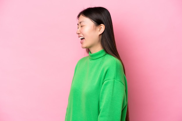 Young Chinese woman isolated on pink background laughing in lateral position