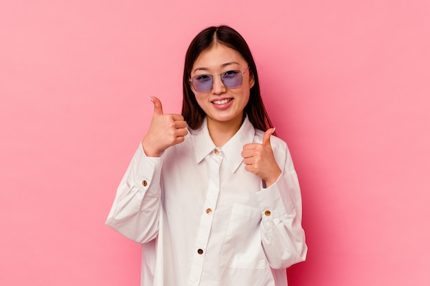 Young chinese woman isolated on pink background raising both thumbs up, smiling and confident.