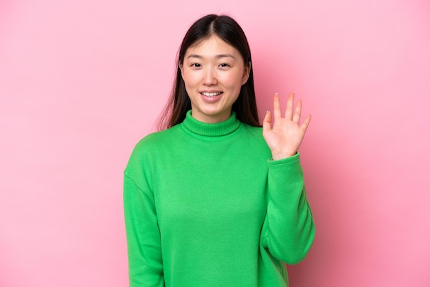 Young Chinese woman isolated on pink background saluting with hand with happy expression