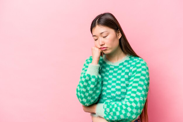 Young Chinese woman isolated on pink background who feels sad and pensive looking at copy space