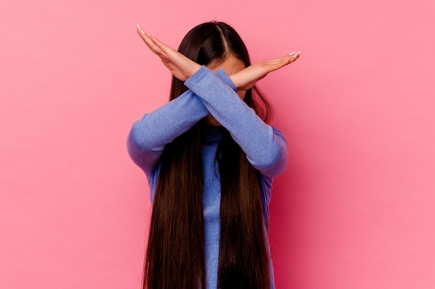 Young chinese woman isolated on pink wall keeping two arms crossed, denial concept.