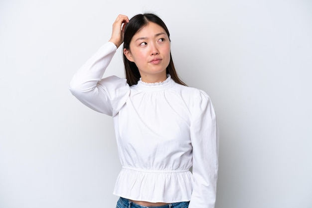 Young Chinese woman isolated on white background having doubts while scratching head