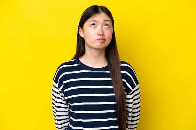 Young Chinese woman isolated on yellow background and looking up