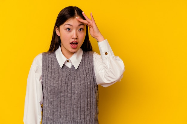 Young chinese woman isolated on yellow background shouts loud, keeps eyes opened and hands tense.