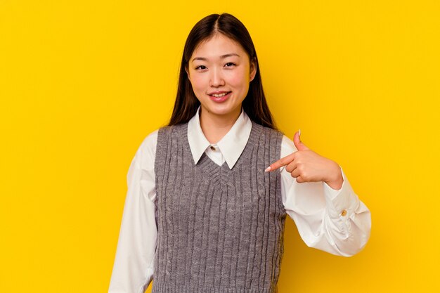 Young chinese woman isolated on yellow wall person pointing by hand to a shirt copy space, proud and confident