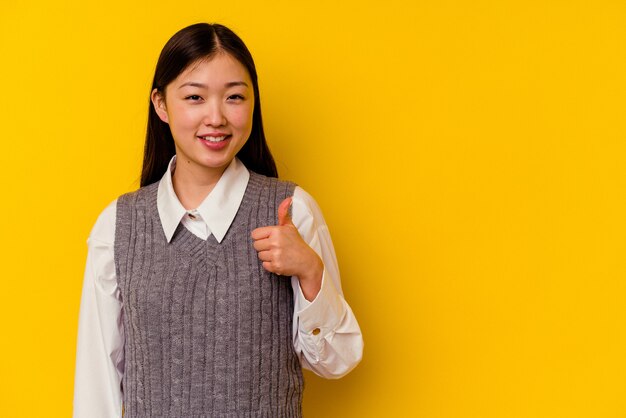 Young chinese woman isolated on yellow wall smiling and raising thumb up