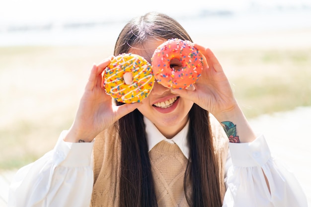 Young Chinese woman at outdoors holding donuts in an eye