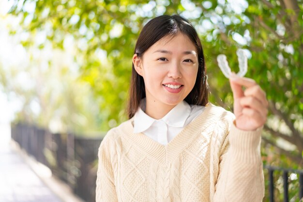 Young Chinese woman at outdoors holding invisible braces with happy expression