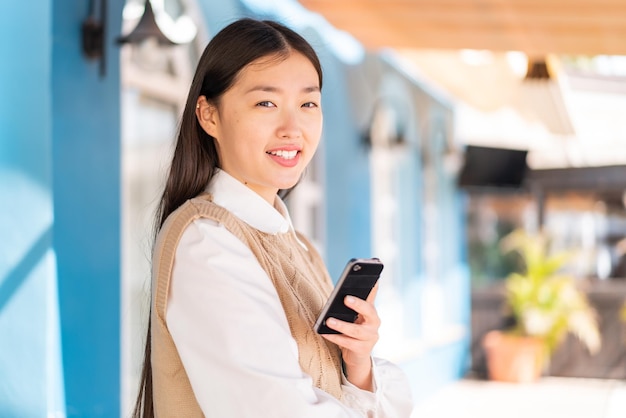 Young Chinese woman at outdoors holding a mobile phone and with arms crossed