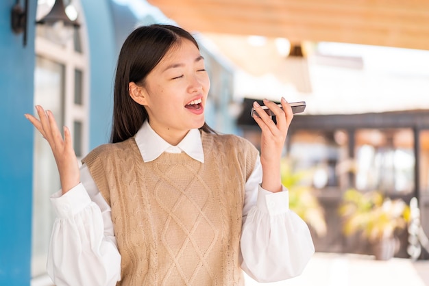 Young Chinese woman at outdoors using mobile phone and singing