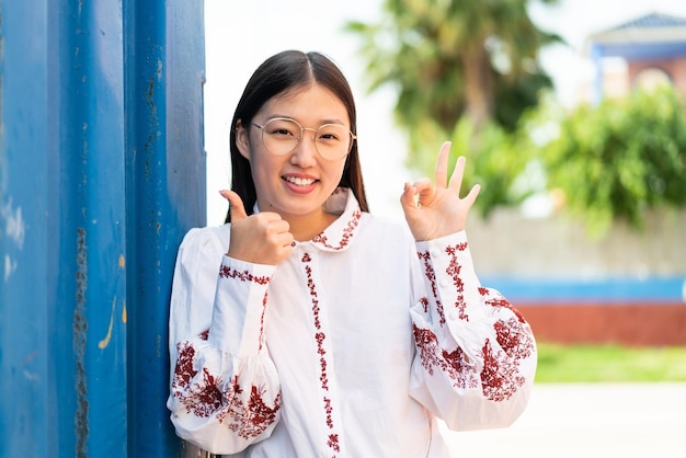 Young Chinese woman at outdoors With glasses and doing OK sign