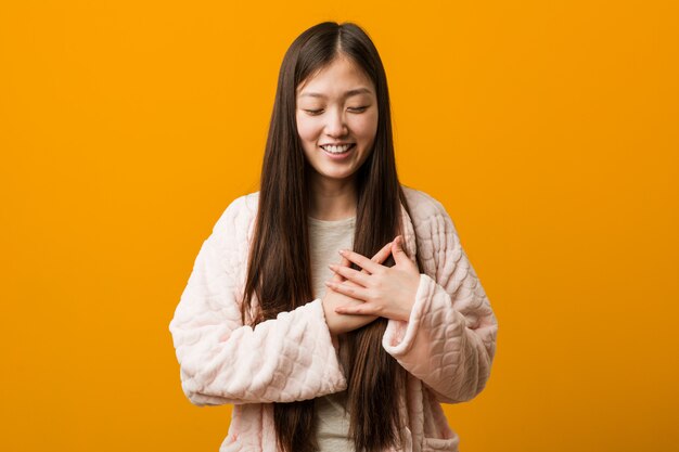 Young chinese woman in pajama laughing keeping hands on heart, concept of happiness.