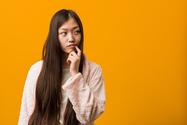 Young chinese woman in pajama looking sideways with doubtful and skeptical expression.