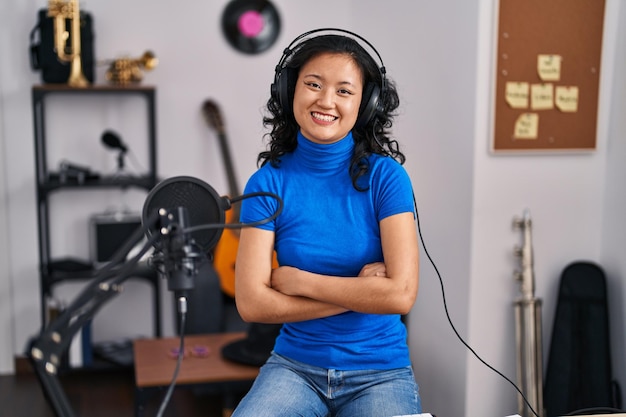 Young chinese woman singer smiling confident with arms crossed gesrture at music studio