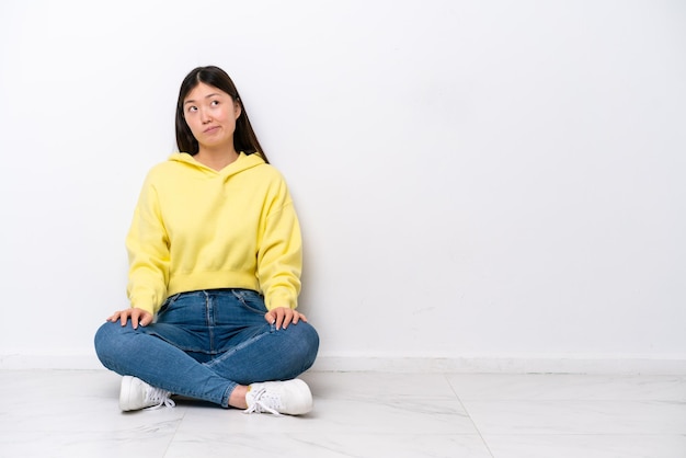 Young Chinese woman sitting on the floor isolated on white wall and looking up