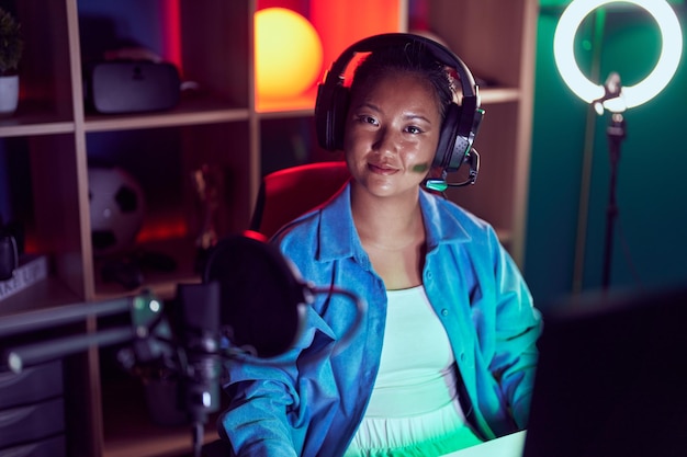 Young chinese woman streamer smiling confident sitting on table at gaming room