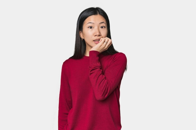 Young Chinese woman in studio setting biting fingernails nervous and very anxious