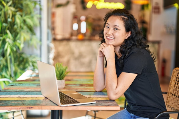 Young chinese woman using laptop sitting on table at restaurant