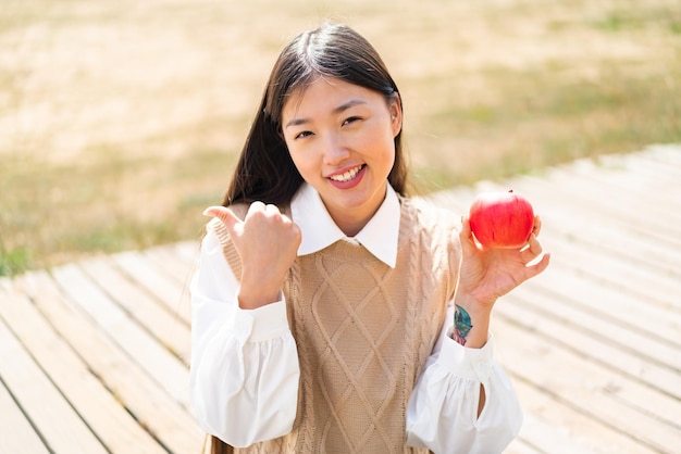 Young Chinese woman with an apple at outdoors pointing to the side to present a product