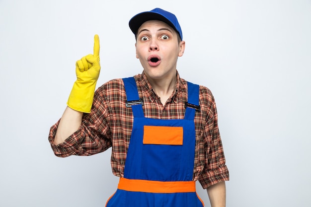 Young cleaning guy wearing uniform and cap with gloves isolated on white wall