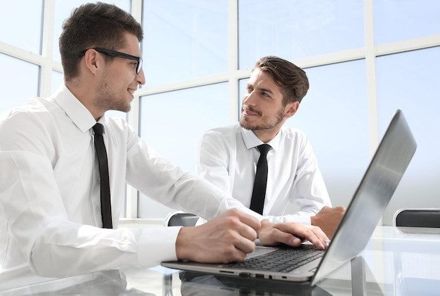 Young colleagues sit at the desk in the office and work on laptops