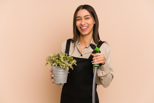 Young Colombian gardener holds a plant and hose, nurturing nature.