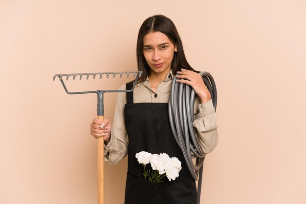 Young Colombian gardener holds a plant and hose, nurturing nature.