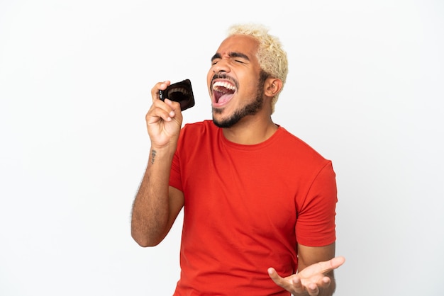 Young Colombian handsome man isolated on white background using mobile phone and singing