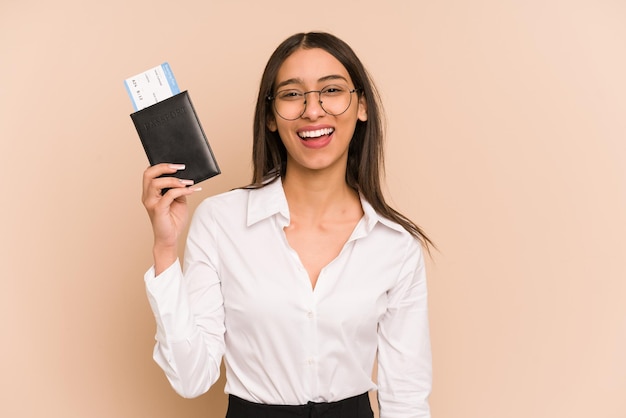 Young colombian woman holding a flight tickets isolated on beige background