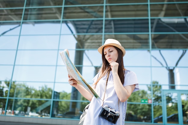 Young concerned traveler tourist woman with retro vintage photo camera looking in paper map, search route at international airport