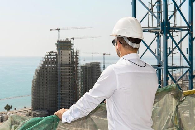 Young confident architect or businessman wearing hard hat looking on a construction site