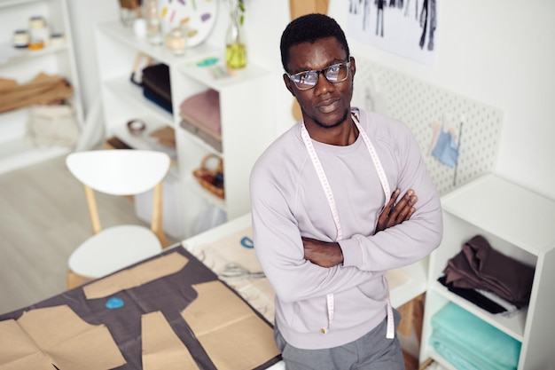 Photo young confident atelier owner standing at table with fabric and cardboard sewing pattern