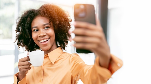 Young confident black woman holding cup posing for selfie